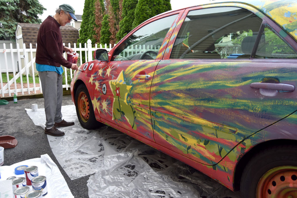 Mark Alston-Follansbee painting his art car in the driveway of his Waltham home, May 28, 2018. (Greg Cook)
