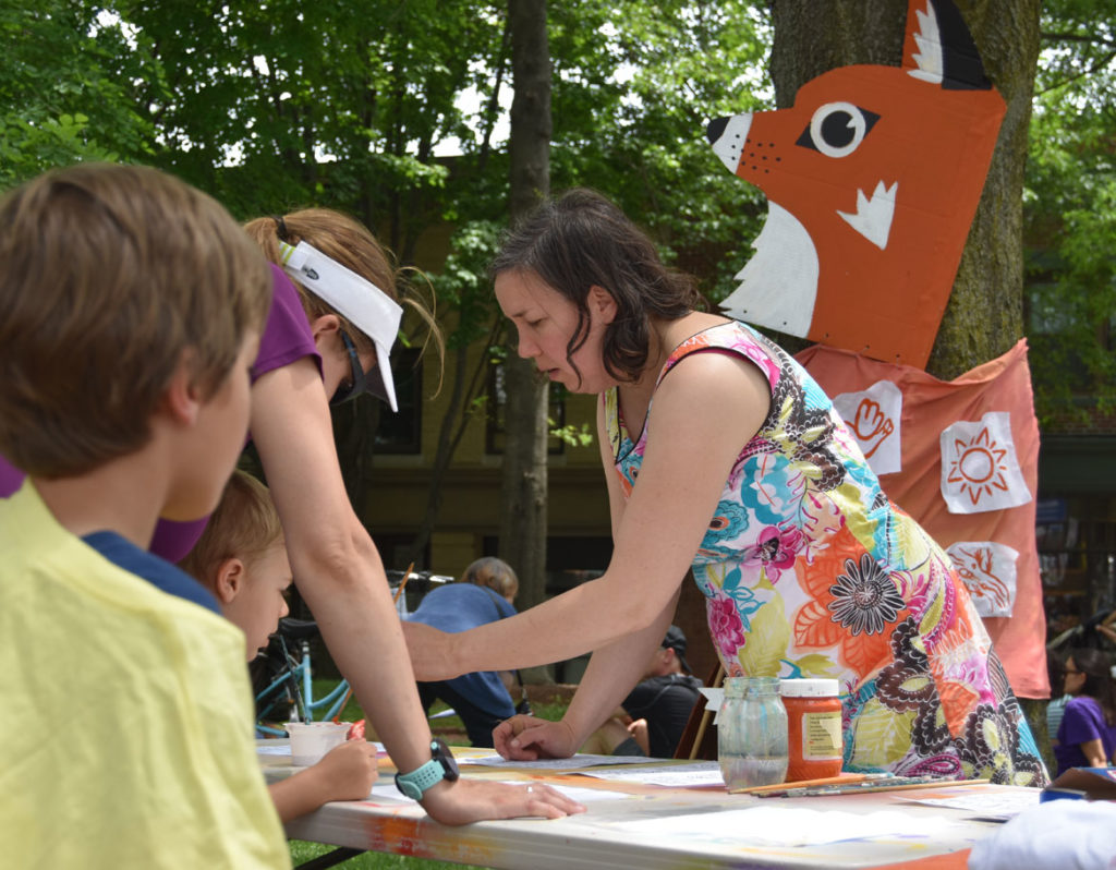 Kari Percival of Wonderland Spectacle Co. works with children to paint patches for a giant fox puppet for Arlington's Fox Festival Parade, June 9, 2018. (Greg Cook)