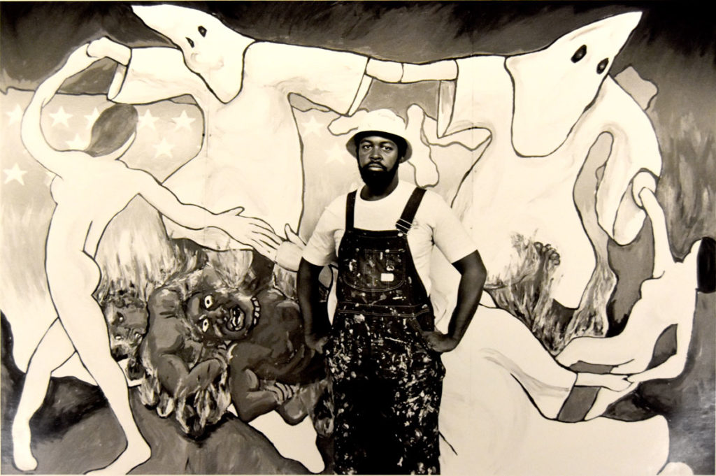 Dana Chandler stands in front of his painting "Sakkkraficial Dance" in a photo promoting its inclusion in the Museum of Fine Arts' 1984 exhibition "Emerging Massachusetts Painters."