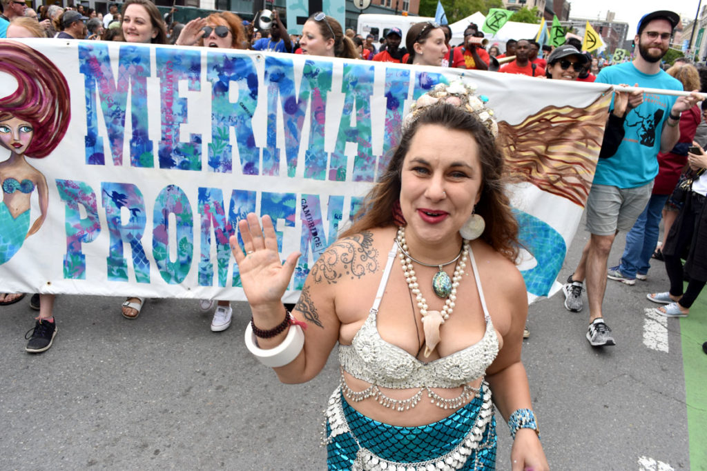 Julz Roth with the banner she made leads the Mermaid Promenade at Cambridge Arts River Festival in Central Square, June 1, 2019. (Greg Cook)