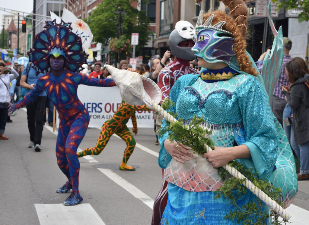 Behind the Mask Studio mermaid followed by Fine Art Superheroes in the Mermaid Promenade at Cambridge Arts River Festival in Central Square, June 1, 2019. (Greg Cook)