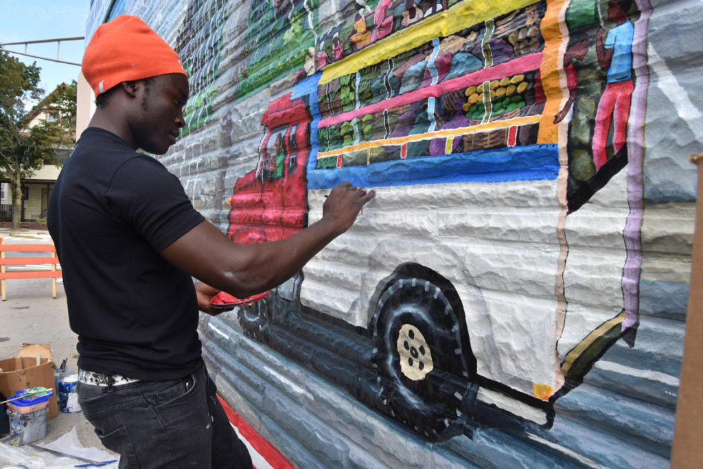 Pascal Michel paints his mural on the side of Highland Creole Cuisine, 2 Highland Ave., Somerville, Aug. 28, 2019. (Greg Cook)