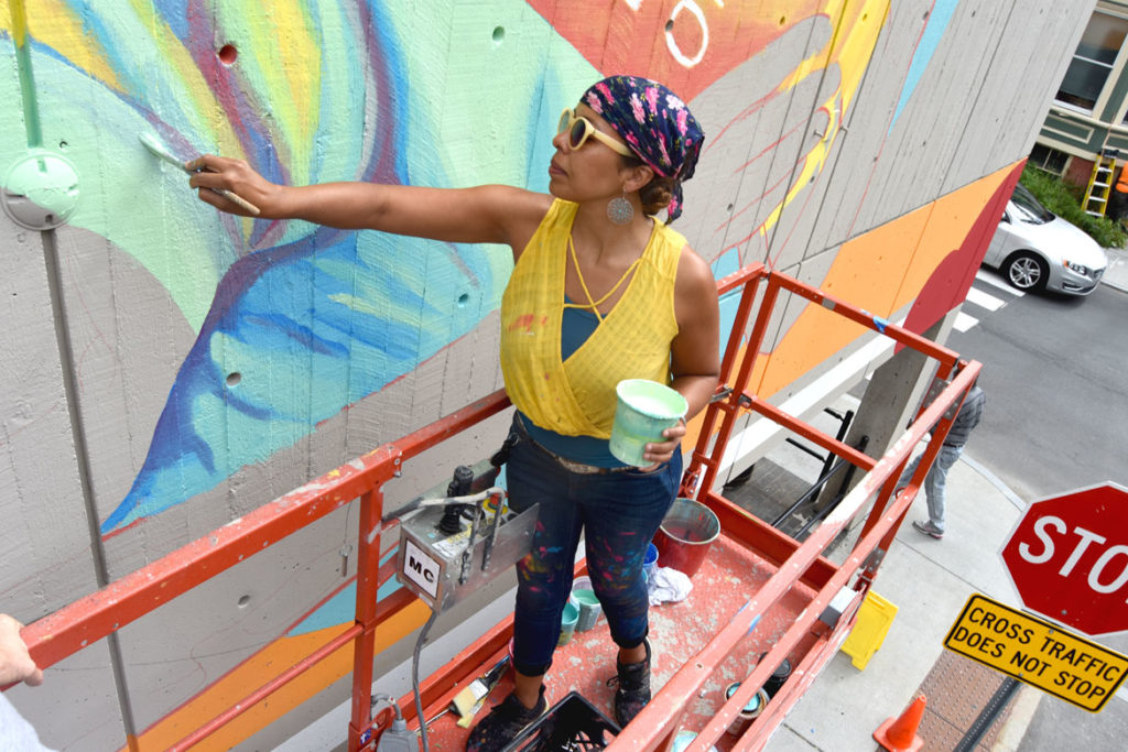 Silvia López Chavez paints a mural on Cambridge's Central Square Library, Aug. 28, 2019. (Greg Cook photo)