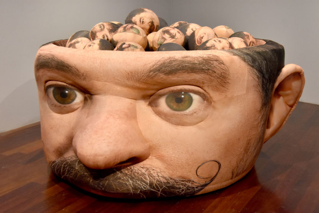Jeffu Warmouth, "Urgent Blowout," 2019, 54-inch-tall, 120-inch long inflatable fabric sculpture filled with 36 inflatable heads, at Boston Sculptors Gallery, Boston, Dec. 13, 2019. (Greg Cook photo)