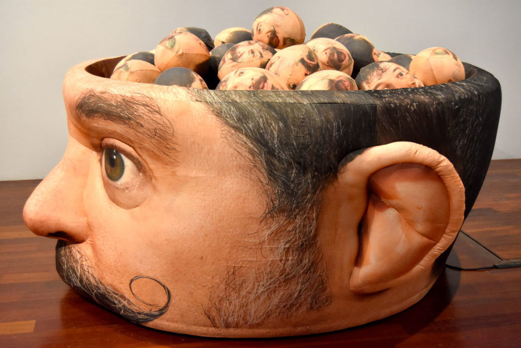 Jeffu Warmouth, "Urgent Blowout," 2019, 54-inch-tall, 120-inch long inflatable fabric sculpture filled with 36 inflatable heads, at Boston Sculptors Gallery, Boston, Dec. 13, 2019. (Greg Cook photo)