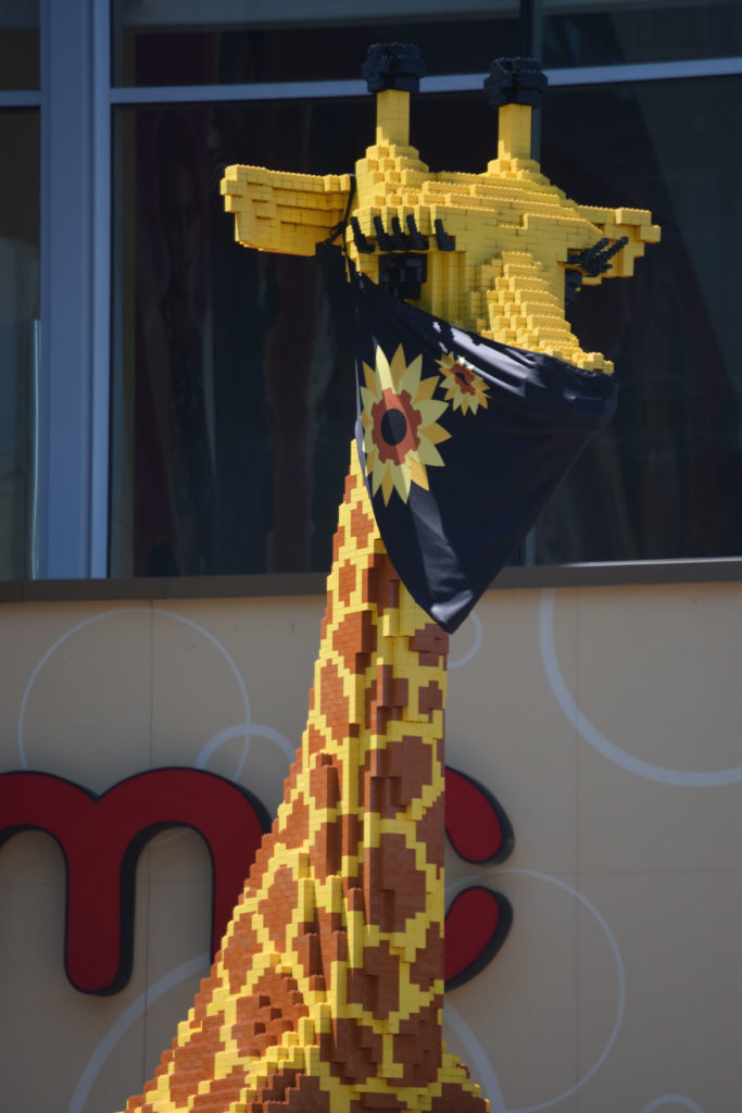 The Lego giraffe standing in front of Somerville's Legoland Discovery Center now wears a coronavirus mask, June 2020. (© Greg Cook photo)