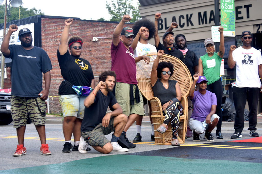 The artists who painted the "Black Lives Matter" street mural on Washington Street in Boston's Nubian Square, surround Black Market owners Chris and Kai Grant (in chair), July 5, 2020. (© Greg Cook photo)