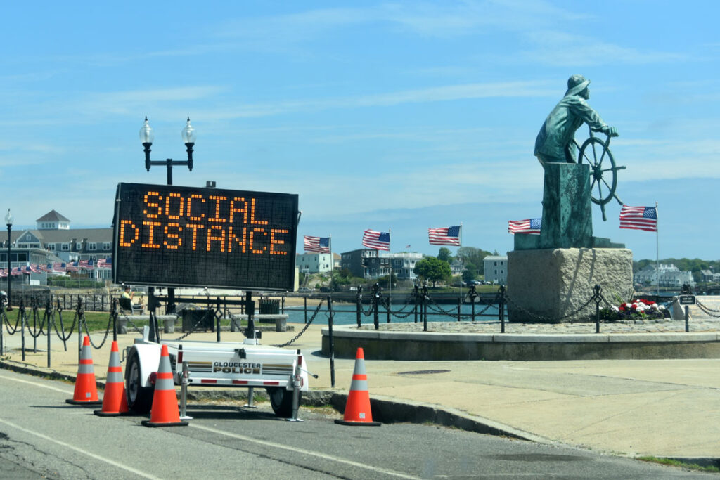 A police sign at Gloucester's Fisherman statue warns to "social distance," May 29, 2020. (©Greg Cook photo)
