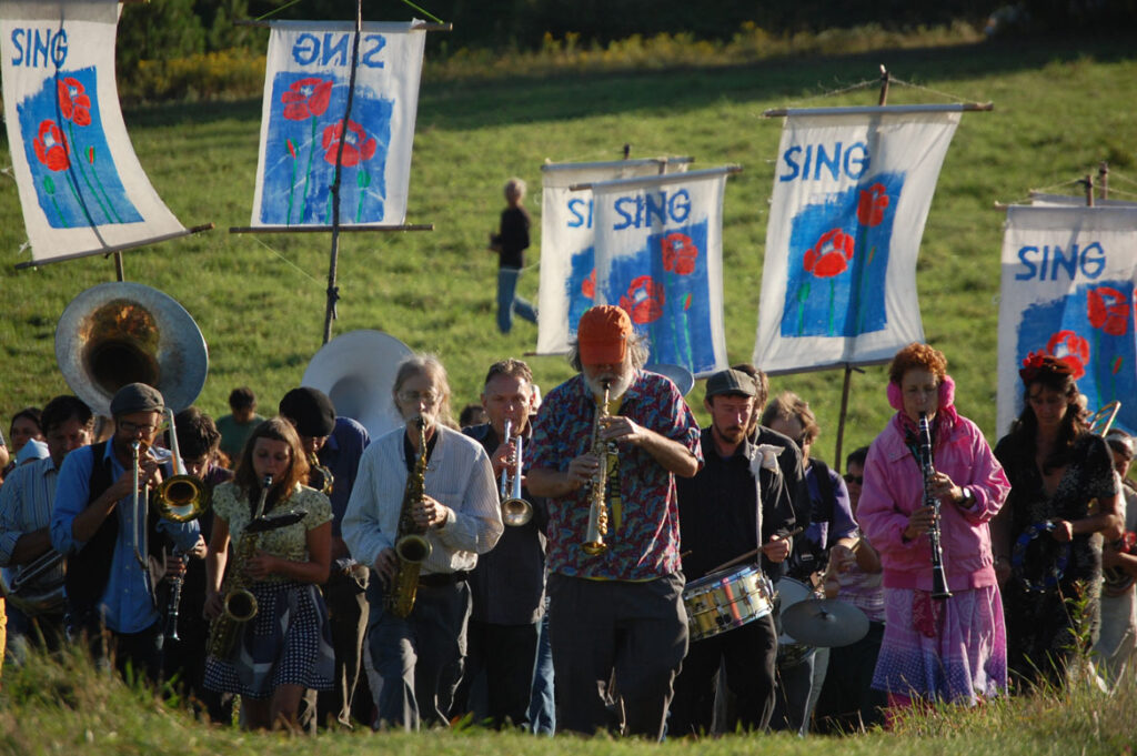 Remi Paillard (far background) photographs the memorial for Pooppy Gregory at the Bread and Puppet farm, Glover, Vermont, Aug. 18, 2012. (©Greg Cook photo)