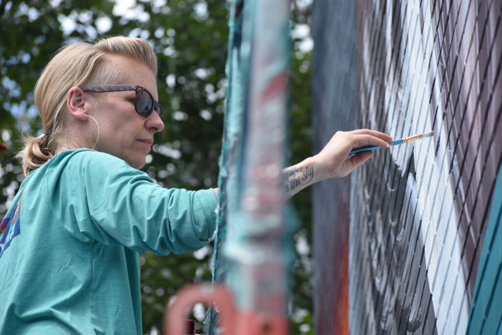 Josie Morway of Boston paints Cunard Tavern, East Boston, for the "Sea Walls" mural project, July 23, 2021. (©Greg Cook photo)