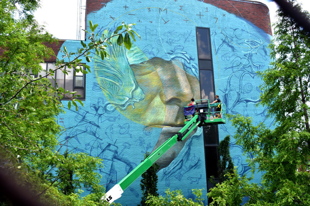 Beau Stanton of New York paints at the East Boston Fire Station for the "Sea Walls" mural project, July 23, 2021. (©Greg Cook photo)