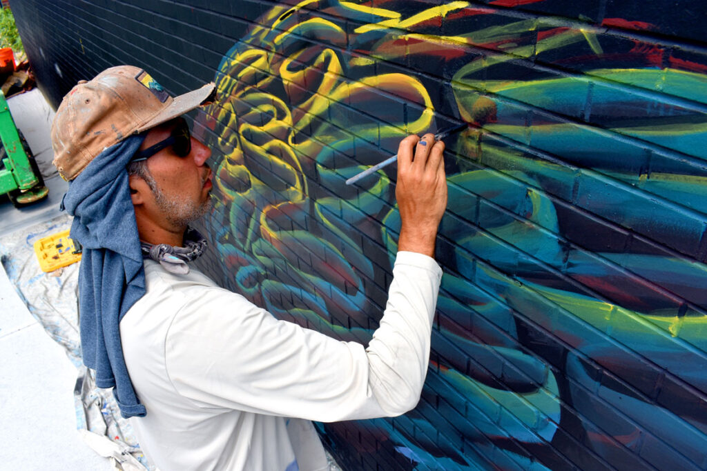 Felipe Ortiz paints at East Boston Early Education Center for the "Sea Walls" mural project, July 23, 2021. (©Greg Cook photo)