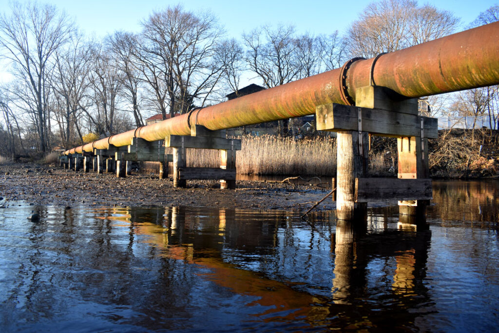 Pipe crosses Saugus River just downstream of Saugus Iron Works, April 8, 2022. (©Greg Cook photo)