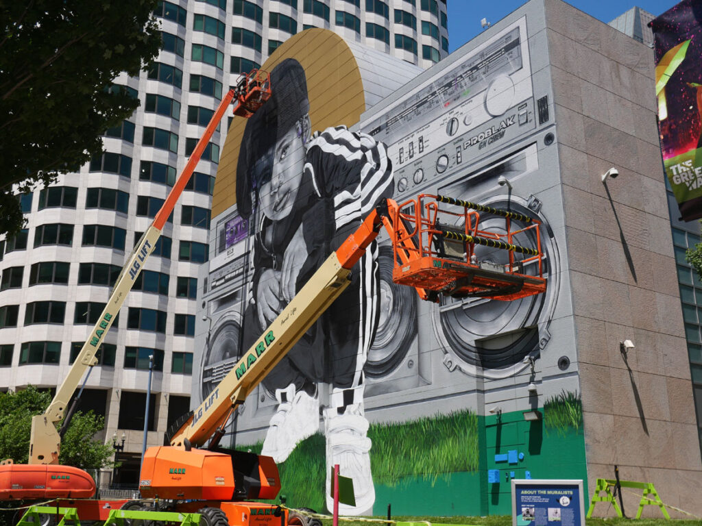 Rob “ProBlak” Gibbs at work on his "Breathe Life Together" mural at Dewey Square on Boston's Greenway, June 14, 2022. (©Greg Cook photo)