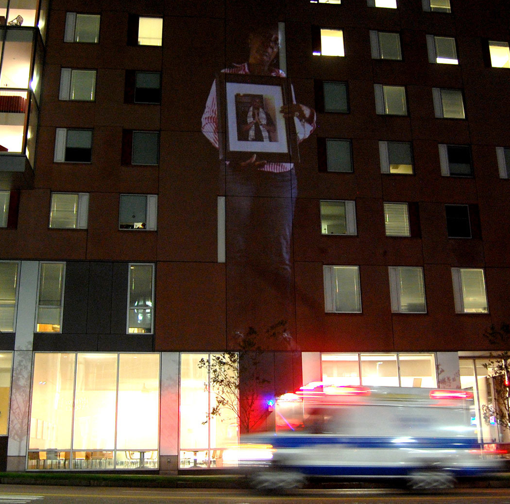 Carla Sheffield is projected onto a Northeastern University building across Ruggles Street from Boston Police Headquarters. (Greg Cook)