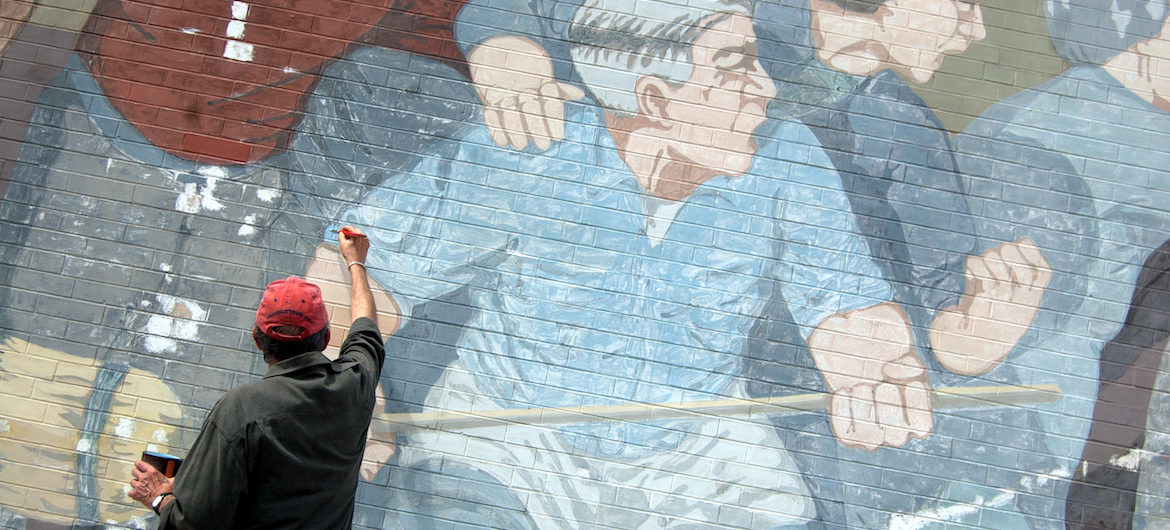 Bernard LaCasse (pictured) works with conservators from the Cambridge Arts Council to restore his iconic “Beat the Belt” mural in Cambridge, June 19, 2017. (Greg Cook)