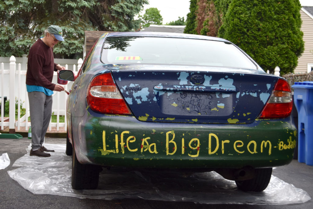Mark Alston-Follansbee painting his art car in the driveway of his Waltham home, May 28, 2018. (Greg Cook)