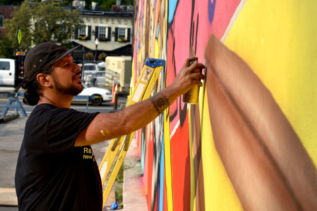 Victor "Marka27" Quiñonez paints his mural "Rebirth" at 2 Union Square, Somerville, Aug. 27, 2018. (Greg Cook)