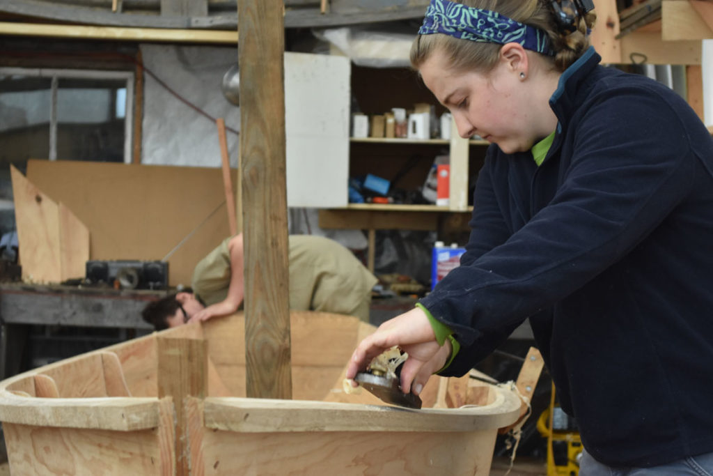 Susannah Winder, Education and Group Program Coordinator, planes an Essex clamming skiff at the Essex Historical Society and Shipbuilding Museum in Essex, April 26, 2018. (Greg Cook)