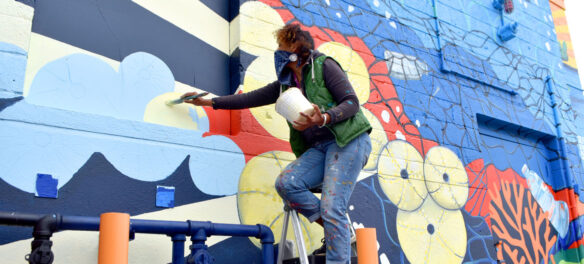 Silvia Lopez Chavez painting her mural for "Sea Walls: Artists for Oceans, Boston 2020," from PangeaSeed Foundation in collaboration with HarborArts at the Boston Harbor Shipyard in East Boston, Sept. 18, 2020. (© Greg Cook photo)