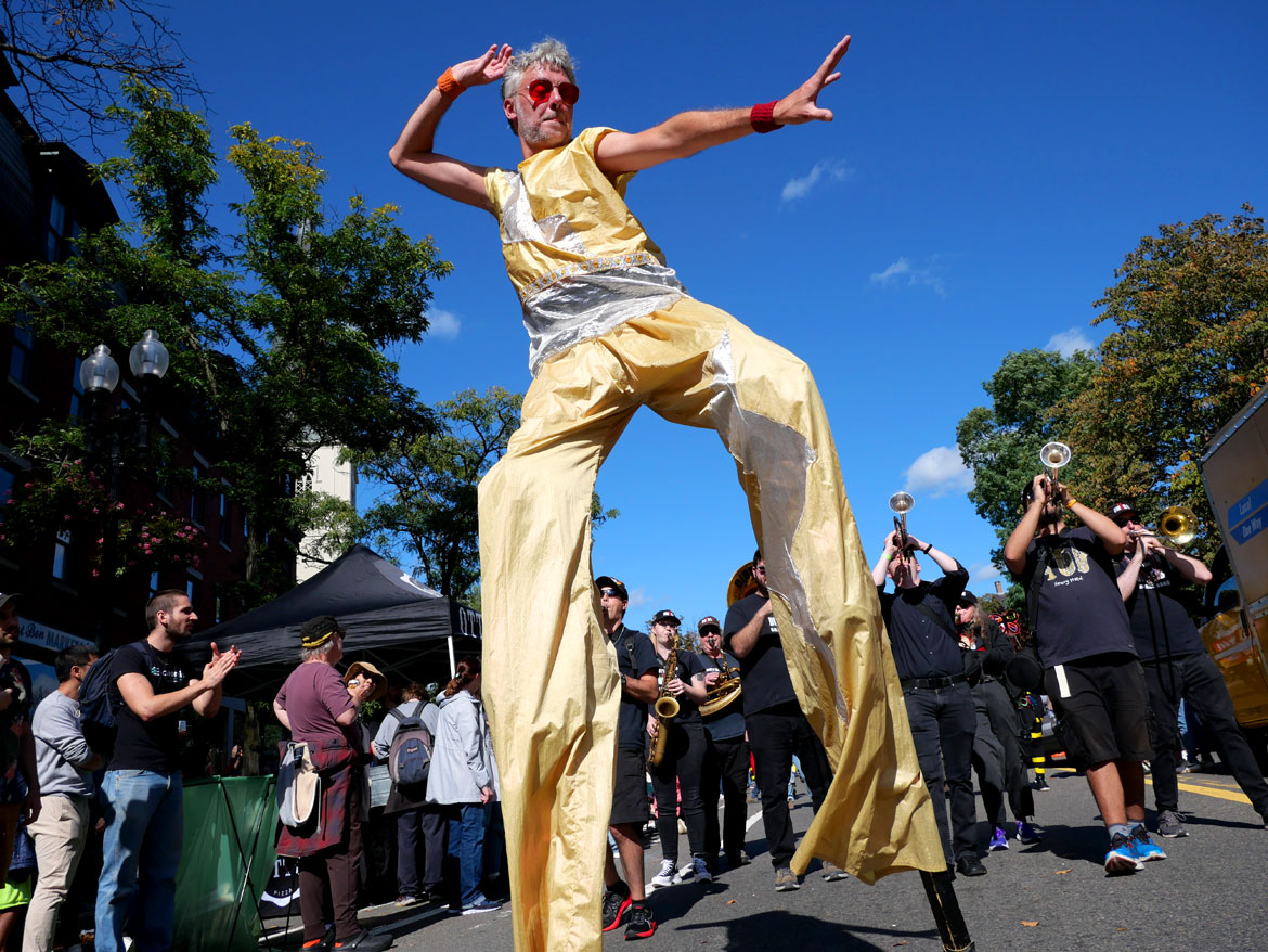 Shawn Morrissey stilts in front of the Dirty Water Bass Band of Boston in the Honk Parade, Oct. 8, 2023. (©Greg Cook photo)