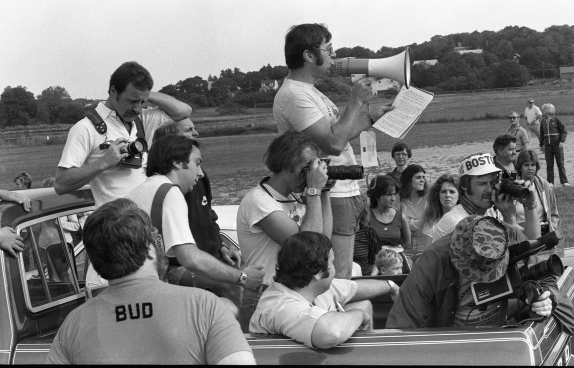 "Gloucester Daily Times employees Jim Mahoney and Jeff Pope fill a truck bed with other photographers ready to capture the Labor Day race," Sept. 6, 1982. Photograph by Jackie Bennett. In "Above the Fold" at the Cape Ann Museum, 2023.