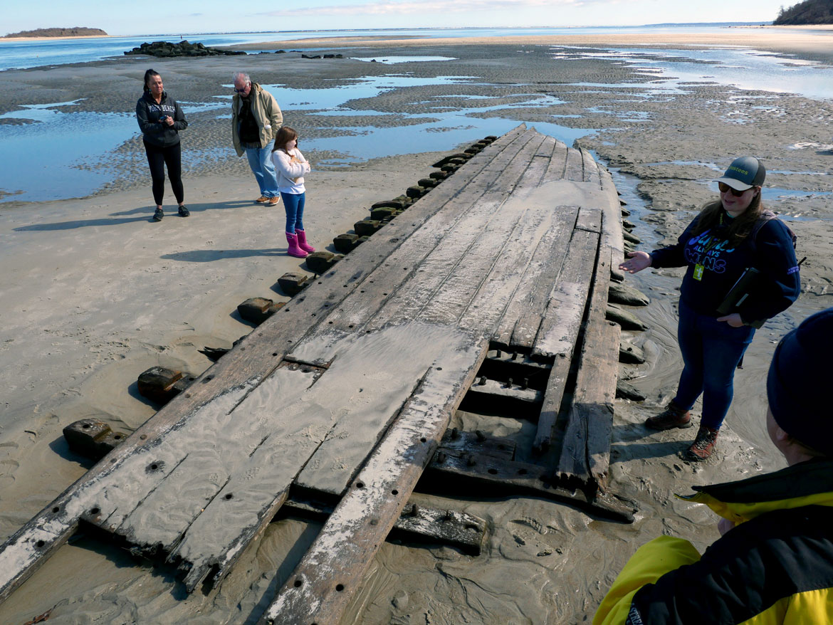 Crane Outdoor Guide Meghan Bowe (right) leads a tour to the shipwreck Ada K. Damon at Steep Hill Beach at The Trustees' Crane Estate, Ipswich, March 16, 2024. (©Greg Cook photo)