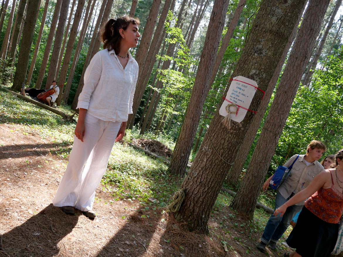 Reading memorials of killed Palestinians and Iranians during Bread and Puppet Theater's "Upside Down World Resurrection Pageant," performed on their Glover, Vermont, farm, July 26, 2026. (©Greg Cook photo)