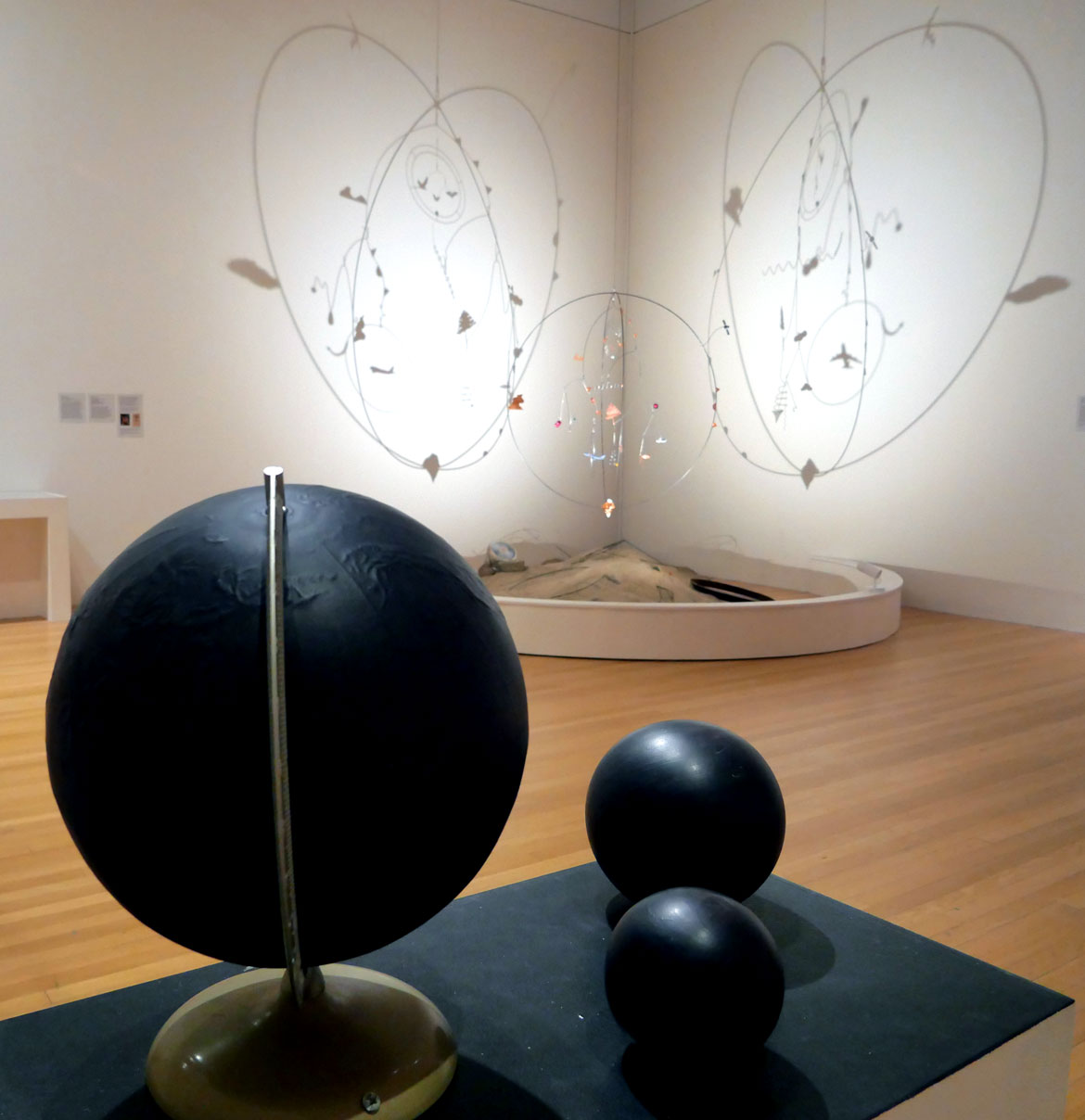 Andrew S. Yang and Christa Donner, "In(Visible) Heat," 2025, wood and cardboard globes with ink and thermochromic paint. In background: Andrew S. Yang, "Earthly Equipoise," 2025. (Greg Cook photo)